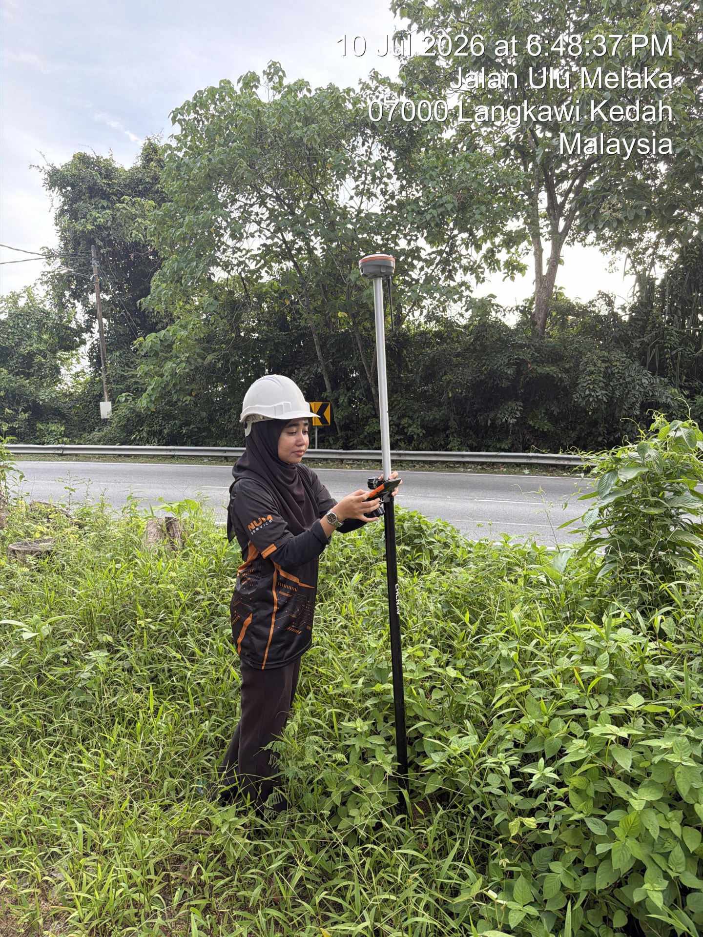 Surveyor operating a GNSS RTK receiver on a roadside verge in Langkawi, Kedah
